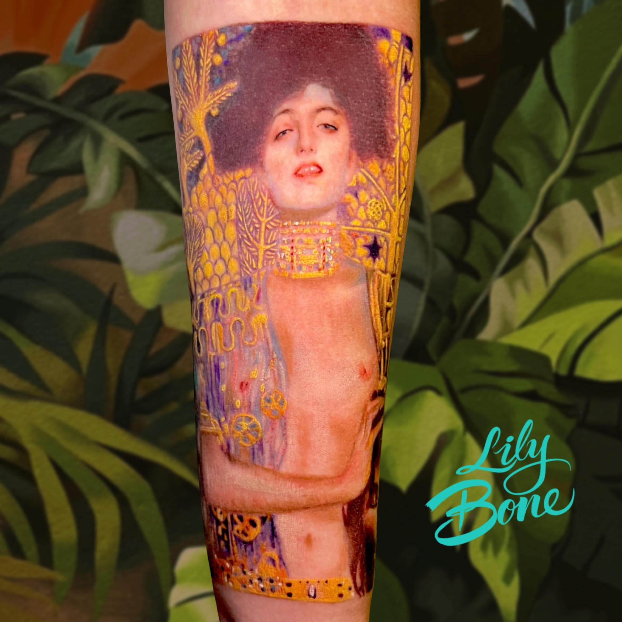 Tatuaje realista inspirado en 'Judith I' de Gustav Klimt, con detalles dorados y estilo pictórico realizado por la tatuadora Lily Bone.